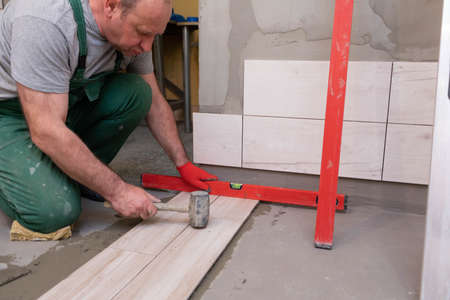 Rubber hammer. An experienced construction worker. Laying terracotta in the bathroom. Work clothes....