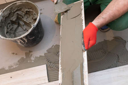 A construction worker lubricates the bottom of the ceramic tile with a metal trowel with special glue.の写真素材