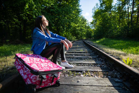 A young woman tired from hiking is sitting on the railway tracks. A holiday adventure without money and on foot all the time.の写真素材