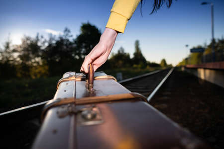 Close-up shots of an old travel suitcase held by the handle by a womans hand while walking along the railroad tracks in the late afternoon...の写真素材