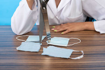 A young medical intern sitting at a desk with tailors scissors in her hand. Destroyed protective...