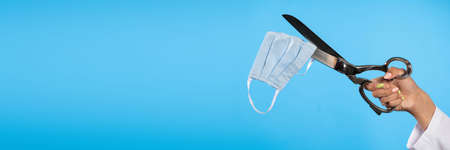 A female hand holds a large tailors scissors and tries to cut the blue protective mask to capture...