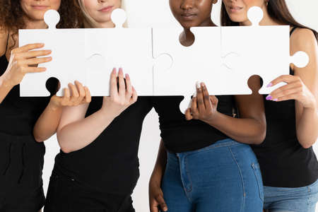 Four different girls hold a puzzle in their hand. Symbolically connecting puzzles as a sign of compatibility and equality of all races.の写真素材