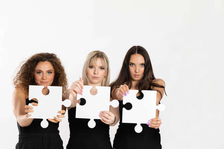Three girls of different races are holding part of a jigsaw puzzle in their hands. At first glance, there are differences, but the puzzles fit together perfectly.の写真素材