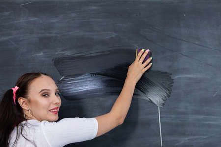 Before the next lesson, the girl wipes the chalkboard with a wet sponge. Her hair is pinned with a pink ribbon in two ponytails.の写真素材