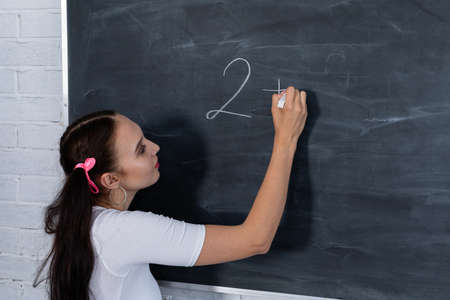 A young schoolgirl writes on the blackboard. School math lesson. He writes a math problem. Girl at a school blackboard.の写真素材
