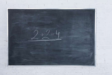 White brick wall. Its written in white chalk on a blackboard - two plus two equals four. The basics...