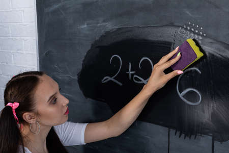 Before the next lesson, the girl wipes the chalkboard with a wet sponge. Her hair is pinned with a pink ribbon in two ponytails.の写真素材