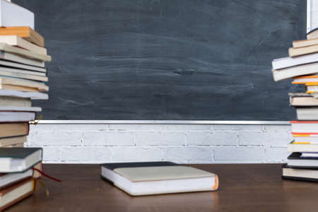 On the background of a school blackboard and a wall made of white bricks, books are stacked on top of each other, forming a high tower. School education is knowledge contained in books.の写真素材