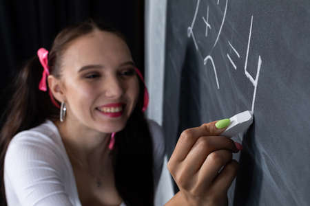 A young schoolgirl writes on the blackboard. School math lesson. He writes a math problem. Girl at a school blackboard.の写真素材