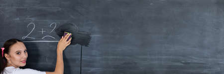 Panoramic style. Before the next lesson, the girl wipes the chalkboard with a wet sponge. Her hair is pinned with a pink ribbon in two ponytails.の写真素材