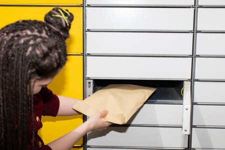 The woman has just received a letter which she is taking out of the mailbox. African braids.の写真素材