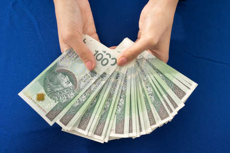 Green banknotes held in young female hands. Blue tablecloth on the table.