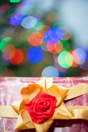 A large red bow on a Christmas gift. A decorative box with a Christmas gift in the background with cork lights.の写真素材