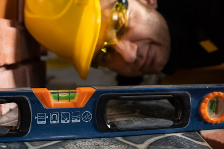 Very close. While laying the terracotta, the general construction worker checks the correctness of execution with a spirit level. An employee wearing personal protective equipment.の写真素材