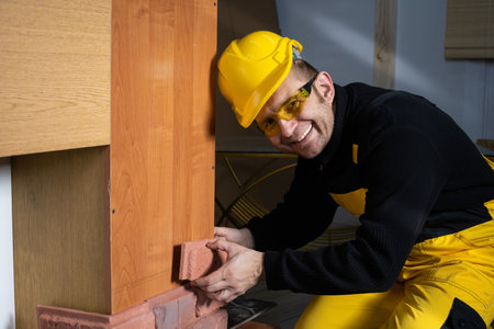 The manual worker tries on a tile to a tile to assess whether it will fit exactly together. An employee dressed in all personal protective equipment.の写真素材