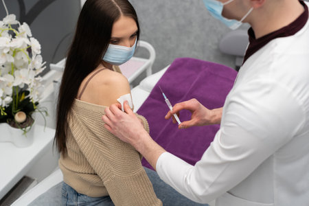A doctor from the infectious diseases ward prepared a vaccine against COVID19 and they intend to inject it into a young patient. A doctors office in a public hospital.の写真素材