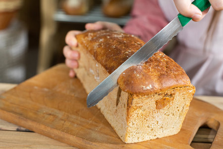 Up close, you can see a young girl starting to cut a loaf of bread with a sharp, clove knife. He...