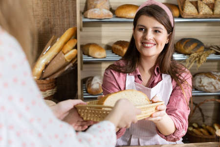 After paying for the bread, an attractive saleswoman serves half a loaf of bread to a young...