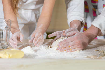 Both girls, mother and five-year-old daughter, knead the cake with their hands on one table, which...