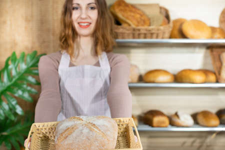 A pretty saleswoman holds a freshly baked loaf of bread in her hands. A multi-generation baking...