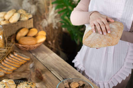 A pretty saleswoman holds a freshly baked loaf of bread in her hands. A multi-generation baking tradition.の写真素材