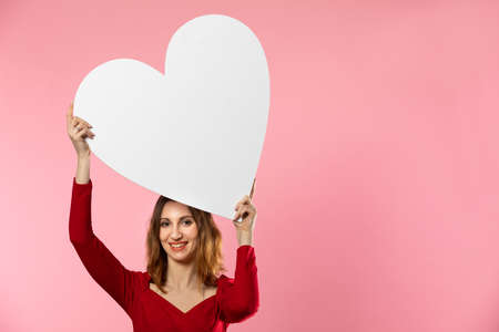 A beautiful girl in love holds a heart shape in her hand. Young woman wants to give a beautiful...