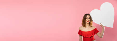 A beautiful girl in love holds a heart shape in her hand. Young woman wants to give a beautiful heart shape as a symbol of love on Valentines Day. In a panoramic frame.の写真素材