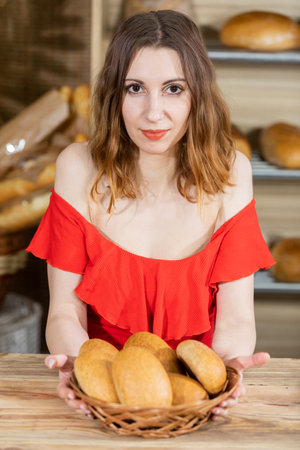 An attractive saleswoman is sitting in her bakery shop holding a basket full of bread in her hands. A multi-generation baking tradition.の写真素材