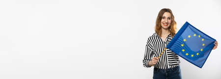 A smiling girl holds in her hand one flag of the European Union. Isolated from the background. A shot in a panoramic frame.の写真素材