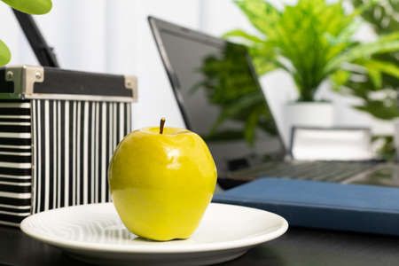 There is a green apple on the employees desk as a vitamin dessert to be consumed during a break from work. Computer workstation for remote work with a tasty incentive.の写真素材