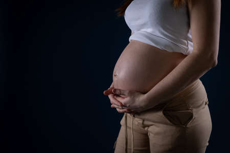 Against a dark blue background, there is a woman with a large belly because she is in the ninth month of pregnancy. Unborn baby in the belly.の写真素材