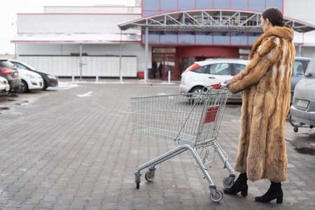 A young girl is walking in the parking lot with a trolley towards the entrance to the supermarket.