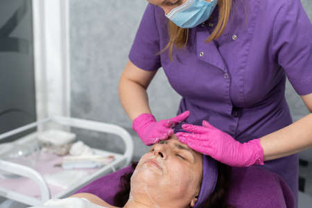 In the first stage, the beautician applies a special gel to the entire face of the client and washes it off with her hands.の写真素材