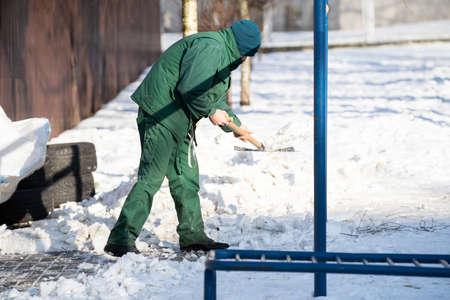 A manual worker scoops snow from the pavement and shovels it onto a pile next to itの写真素材