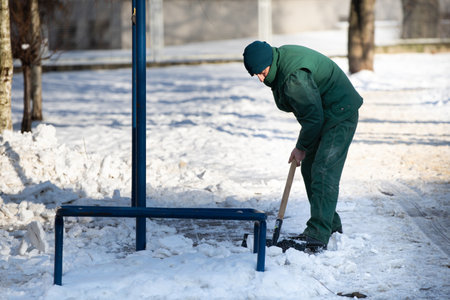 A manual worker scoops wet snow and ice on a shovelの写真素材