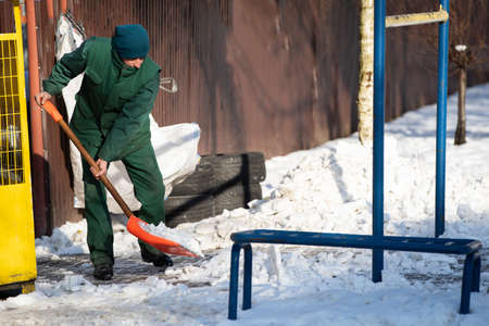 A manual worker scoops snow from the pavement and shovels it onto a pile next to itの写真素材