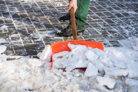 A manual worker scoops wet snow and ice on a shovel