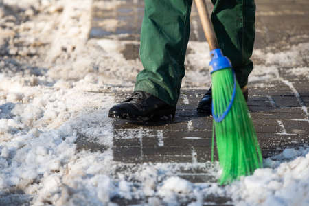 A close-up view as a worker sweeps the pavement out of loose snowの写真素材