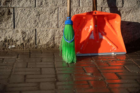 An orange snow shovel and a stick brush are leaning against the wallの写真素材