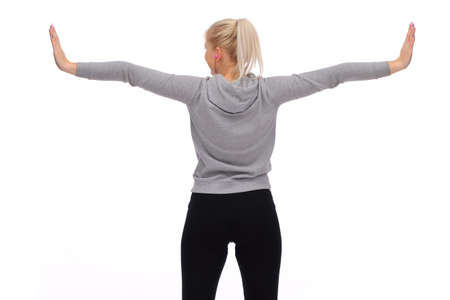 While exercising, a young girl spreads her arms to the sides and looks to the side. Rear view