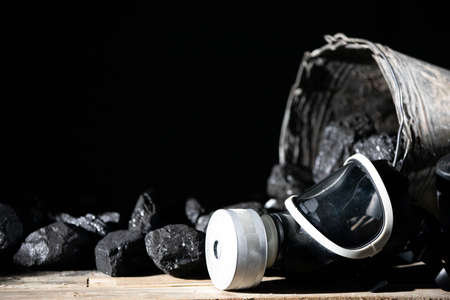 A gas mask lies on a wooden platform against a background of black coalの写真素材