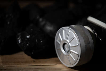 A gas mask with a filter lies on a wooden platform against a background of planks and black charcoalの写真素材