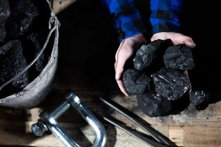A miner holds small lumps of black coal in his hands over a wooden platformの写真素材