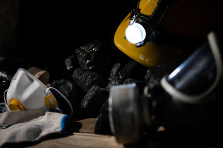 A protective helmet with a glowing flashlight and a dust mask with a filter lie on top of the black coalの写真素材