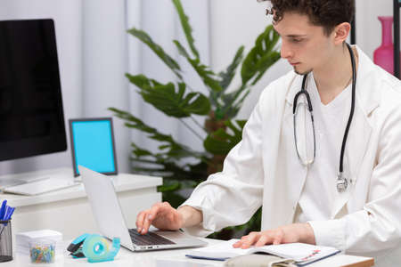 A young primary care physician enters patient data into a laptop database. Doctors office