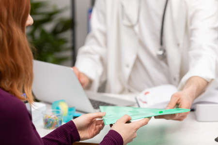 A patient with red hair gives medical records to her family physician. Doctors office. Close-up view