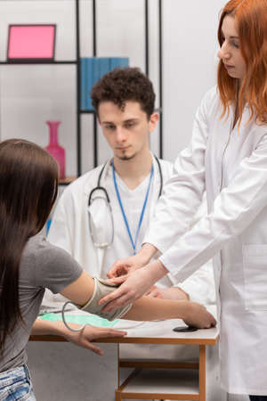 A red-haired nurse puts a blood pressure monitor on a young patients arm. Primary care physician. Doctors officeの写真素材