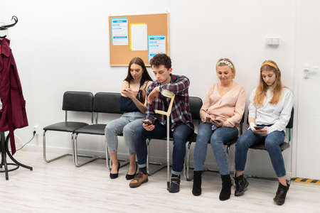 Patients sit in a clinic waiting for their turn to go to the doctors office. They look at their cell...
