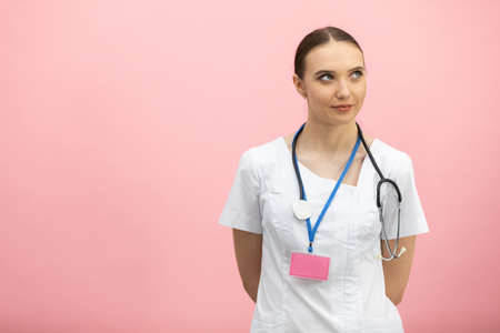 A smiling lady doctor in a white apron stands against a pink background.の写真素材